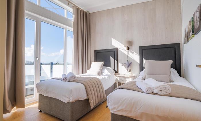 Two full size single beds with grey fabric headboards and beige curtains and bed runners, a rhino head bedside lamp and rhino canvasses on the wall.